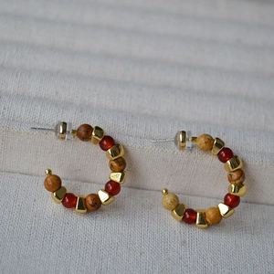 Macro detail of vintage C-shaped earrings with red natural stones and gold metal spacers