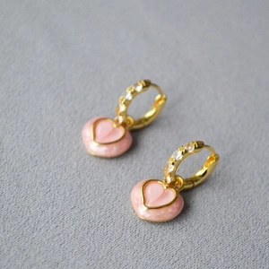 Boucles d'oreilles cœur rose avec placage or et cristaux brillants sur fond de tissu