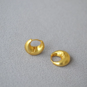 Detail of matte gold chunky hoop earrings with a textured surface and secure clasp closure