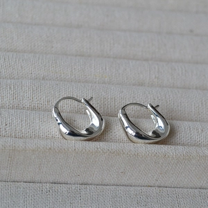 Close-up of silver irregular U-shaped chunky earrings on a beige textured tray