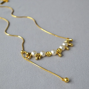 Dettaglio della collana lunga dorata con perle bianche e inserti in metallo