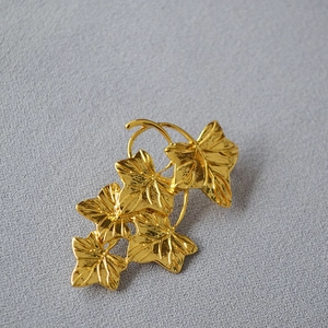 Vintage golden ivy leaf brooch with textured metal finish on soft grey fabric