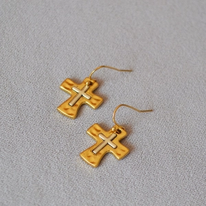 Detail of vintage brass cross earrings with hammered texture and two-tone metal finish