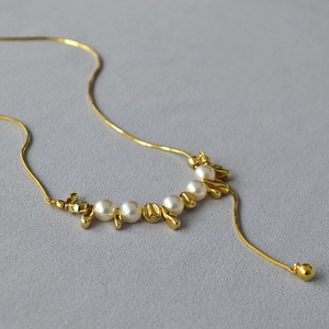 Dettaglio di una collana a catena serpente con cinque perle bianche e accenti in metallo oro
