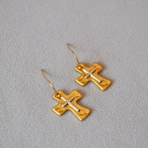 Macro shot of two-tone gold and silver cross earrings on gray textured fabric background