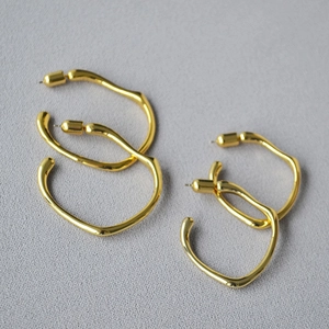 Detailed close-up of polished golden irregular wavy hoop earrings on a grey background