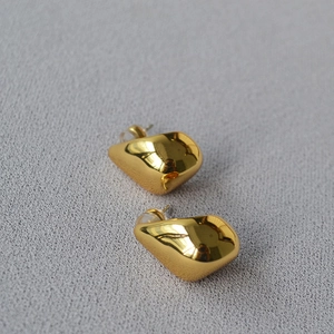 Detailed close-up of shiny gold droplet stud earrings on textured gray fabric