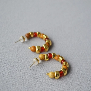 Macro detail of Bohemian C-shape hoop earrings with gold, marble stone and red beads
