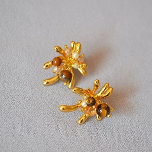 Macro shot of gold-plated earring with tiger eye, pearls, and fireworks design