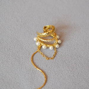 Detail of gold ear cuff with lattice texture, faux diamonds, pearls, and chain fringe
