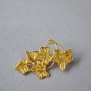Detail of vintage gold metal brooch featuring intricate vine leaf patterns and texture