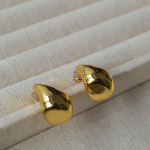 Macro view of gold teardrop clip-on earrings on a white textured jewelry tray