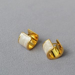 Détail macro de boucles d'oreilles en laiton doré avec incrustation émail nacré blanc