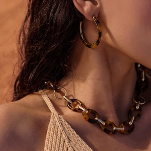 Close-up of retro tortoiseshell resin hoop earrings and thick chain necklace on model