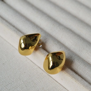 Detail of high-polish irregular teardrop earrings on a beige textured jewelry tray