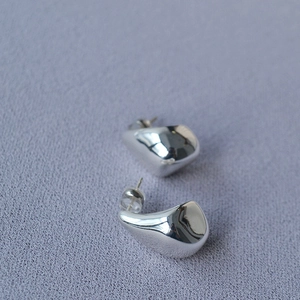 Close-up of irregular teardrop earrings in polished silver finish on textured fabric