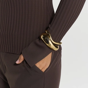 Detailed view of irregular wavy gold-plated brass cuff bracelet on model's wrist