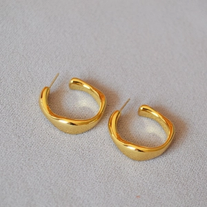 Detail of polished gold-plated irregular C-shape hoop earrings with a mirror finish
