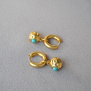 Vintage textured gold hoop earrings with turquoise spheres on grey fabric background