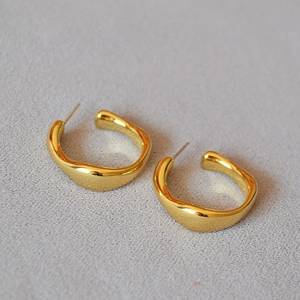 Macro detail of gold plated irregular C-shape hoop earrings with a polished wavy texture