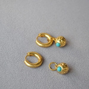 Detail of detachable gold hoop earrings with turquoise stones and textured metal spheres
