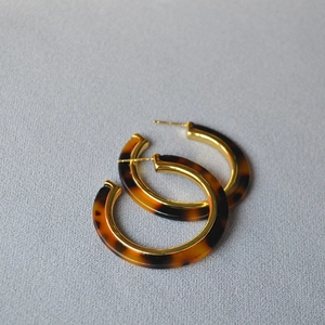 Detailed close-up of retro C-shaped earrings with tortoiseshell resin and gold metal inlay