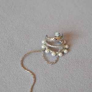 Close-up of layered silver ear cuff with quilted pattern, crystals, and pearl tassel