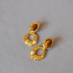 Détail macro de boucles d'oreilles en laiton avec œil de tigre et texture de lave