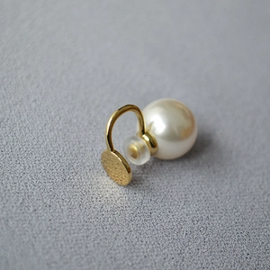 Détail d'un clip d'oreille doré avec une perle brillante et un disque au fini mat brossé