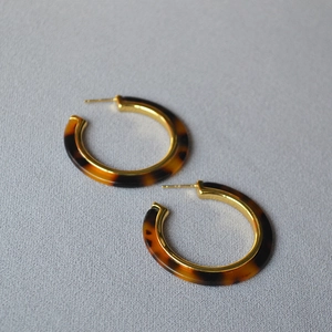 Detail of C-shaped resin hoop earrings featuring tortoiseshell pattern and gold inner metal