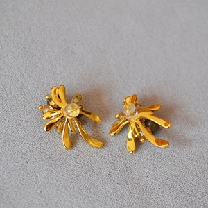 Macro view of gold flower earrings featuring tiger eye beads on gray fabric background