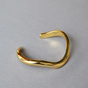 Macro view of polished gold wavy bangle with irregular fluid lines on gray background
