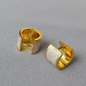 Détail de boucles d'oreilles créoles dorées en laiton avec émail marbré blanc