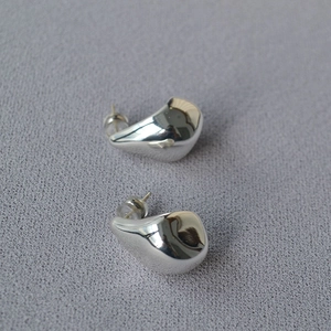 Macro detail of silver-tone teardrop earrings on textured grey fabric background