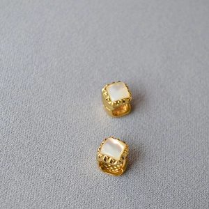 Detail of square brass earrings with white mother of pearl inlay and gold textured edges