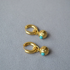 Detail of vintage textured gold orb earrings with inset turquoise bead against a gray fabric