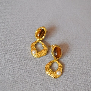 Vue détaillée des boucles d'oreilles en laiton doré avec oeil de tigre et perle blanche
