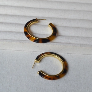 Close-up of C-shaped resin leopard print earrings on a beige textured jewelry display base