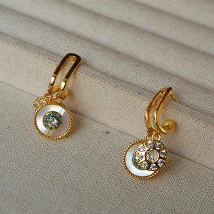 Macro detail of gold-tone drop earrings featuring white mother of pearl and blue zircon stones