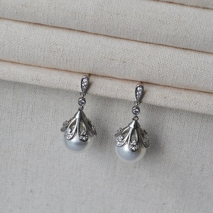 Macro detail of silver pearl earrings with crown bracket and sparkling zircon stones