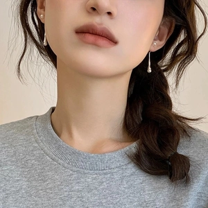 Close-up of minimalist silver teardrop earrings with a small pearl stud on a model