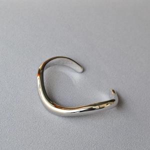 Macro shot of silver irregular wavy open bangle with high-polish mirror finish surface