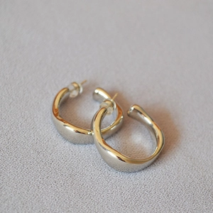 Macro shot of irregular silver-plated C-shape hoop earrings with high-polish mirror finish