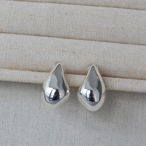Macro shot of minimalist silver teardrop stud earrings with a polished mirror finish surface