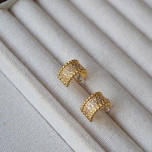 Detailed close-up of C-shaped gold-plated wide hoop earrings with paved cubic zirconia stones