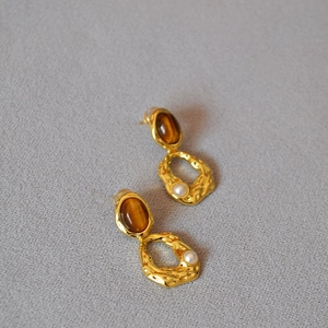 Détail de boucles d'oreilles dorées avec œil de tigre, texture martelée et perles