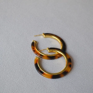 Close-up of retro tortoiseshell resin C-shaped hoop earrings with gold metal frame