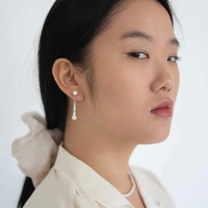 Detail of silver drop earrings with white pearls on a model in a minimalist studio setting