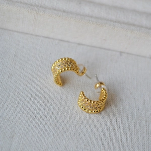 Elegant gold C-shaped hoop earrings with pave set sparkling zircons on textured linen cloth