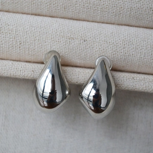 Macro shot of polished silver teardrop earrings resting on a textured cream jewelry stand